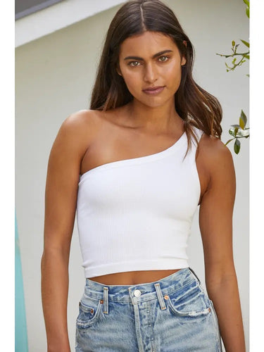 Model wearing the Minuett Top in white featuring a fitted ribbed knit construction, asymmetrical one-shoulder neckline, and cropped silhouette, paired with light-wash denim jeans.