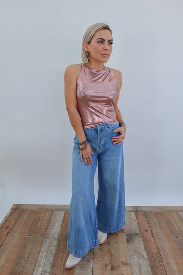 Model wearing the Alameda Sleeveless Top — rose gold metallic high-neck sleeveless blouse styled with wide-leg denim for a chic, modern look.