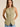 Model wearing the Muse Vest in soft sage green featuring a tailored fitted silhouette, button-front closure, pointed hem, sleeveless cut, and decorative flap pockets paired with light wash denim jeans.