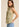 Side view of the Muse Vest in soft sage green showcasing the tailored fit, sleeveless silhouette, button-front design, and pointed hem styled with light wash jeans.