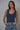 Model wearing the Nightjar Top in deep blue featuring a sleeveless fitted silhouette, classic scoop neckline, soft stretch knit fabric, and body-skimming fit styled with high-waisted blue jeans.