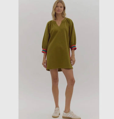 A model wearing an olive green dress with puffed sleeves and red and teal side stripes, paired with white sneakers.