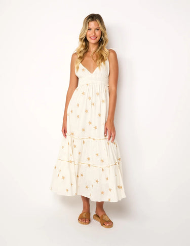 "Woman wearing an ivory midi dress with gold star embroidery, sleeveless V-neck, tiered skirt, styled with tan sandals – summer resort fashion"
