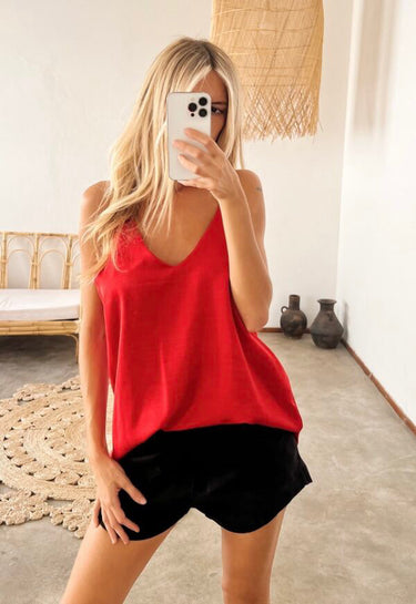 Model wearing the Terra Top in red — silk V-neck tank, relaxed fit, paired with black shorts, minimalist resort look.