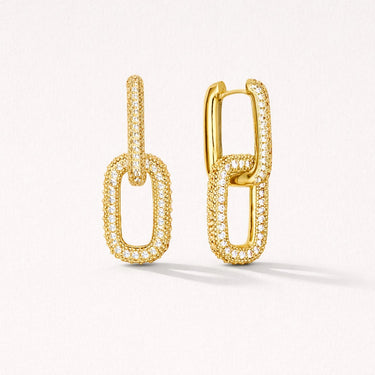 Risha Huggie Earrings in gold featuring elongated interlocking links with pavé cubic zirconia detailing, displayed on a soft light gray background with subtle shadow, modern lightweight drop earrings