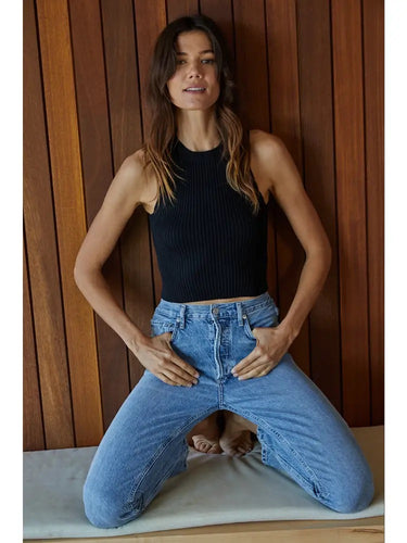 Model wearing the black Romett Top with a ribbed knit texture, mock neckline, sleeveless cut, fitted cropped silhouette, and relaxed light-wash denim jeans.