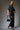 Woman wearing the Roux Top in charcoal black with sculpted ruching and dramatic draped detail, styled in soft natural light on a neutral background.