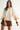 Sienu Sweater in cream featuring a relaxed oversized knit silhouette with cape sleeves, decorative button details, and a soft draped fit paired with a brown mini skirt.