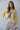 Syrat Sweater in butter yellow featuring a relaxed oversized knit silhouette with a colorful embroidered bird motif, ribbed trim, and soft lightweight fabric paired with neutral corduroy pants.