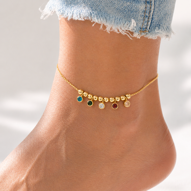 Model wearing Syrath Anklet gold anklet with multicolor crystal charms and dangling bead details.