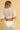 Model wearing the Tottem Crop Top in white — cotton eyelet fabric, cropped silhouette, V-neck, wide sleeves, paired with matching pants, resort look, back view.