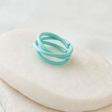 Turquoise adjustable ring with intertwined bands displayed on a beige stone background – Celeste Adjustable Ring by Matte