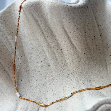 Unify Necklace by Matte, gold plated chain with white beads on cream textured surface