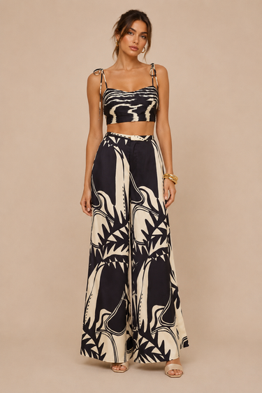 Woman wearing the Vittoria Set featuring a black and ivory abstract print, adjustable tie-shoulder cropped top, high-waisted wide-leg pants, lightweight woven fabric, and a relaxed resort-inspired silhouette.