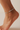 white anklet with a small charm on a foot against a neutral background