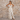 Matte All Dresses collection image – model wearing a cream tropical-print maxi dress in front of a textured beige stone wall in warm natural sunlight