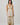 Matte All Dresses collection image – model wearing a cream tropical-print maxi dress in front of a textured beige stone wall in warm natural sunlight