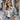 Model wearing a metallic silver outerwear jacket from the Matte Outerwear Collection, styled with rolled sleeves, white tank top, and denim jeans on a city street.
