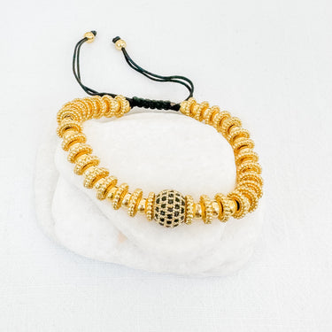 A gold-colored adjustable bracelet with a mix of round and link chains, featuring a spherical charm with a black and white pattern.
