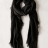 Black lightweight scarf with fringe edges folded on neutral linen background.
