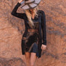 Woman wearing Andrea Mini Dress in black sheer fabric and beaded design against desert background.