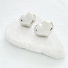Silver heart-shaped stud earrings displayed on white marble stone, minimalist jewelry photography, Angelina Stud Earrings by Matte.
