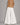 Annalise Jean– Back view of white wide-leg palazzo jeans featuring a high-rise waist, oversized flowing legs, clean white denim, square back patch pockets with double topstitching, tonal stitching throughout, and a full-length dramatic silhouette. Styled with a camel faux leather blazer and neutral heels.

