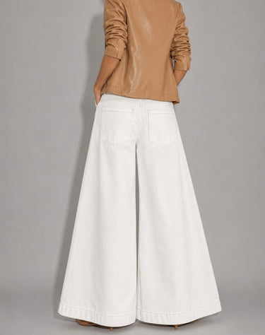 Annalise Jean– Back view of white wide-leg palazzo jeans featuring a high-rise waist, oversized flowing legs, clean white denim, square back patch pockets with double topstitching, tonal stitching throughout, and a full-length dramatic silhouette. Styled with a camel faux leather blazer and neutral heels.
