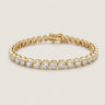 Gold bezel tennis bracelet with round clear stones, polished silver finish, secure clasp closure, and minimalist luxury jewelry styling on a warm light gray background.
