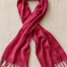 Fuchsia pashmina scarf with soft fringe edges folded on beige linen background.

