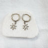 A pair of gold-plated huggie earrings with star charms attached, displayed on a white surface.