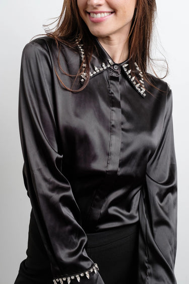 Woman in black satin Astra Crystal Blouse with sparkling crystal collar and cuff accents, styled with tailored black pants.