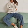 Woman wearing relaxed neutral sweatshirt with dropped shoulders and ribbed cuffs, styled with blue jeans and sneakers.