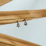 A pair of gold-plated huggie earrings with star designs, displayed against a wooden backdrop.