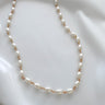 A gold-filled necklace with white pearls, displayed on a white surface.