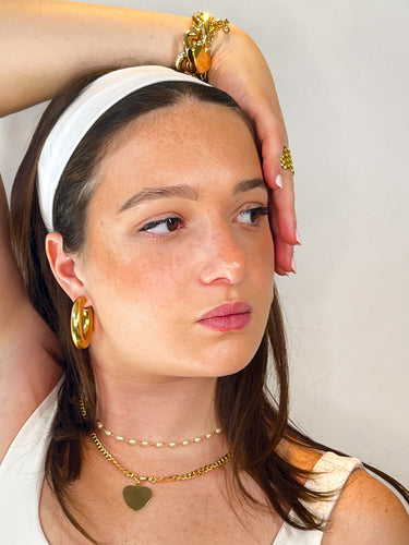 Woman wearing gold jewelry including earrings, necklaces, and bracelets against a neutral background