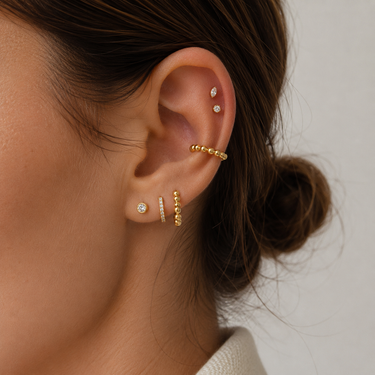 Close-up of an ear wearing gold and diamond earrings with a neutral background