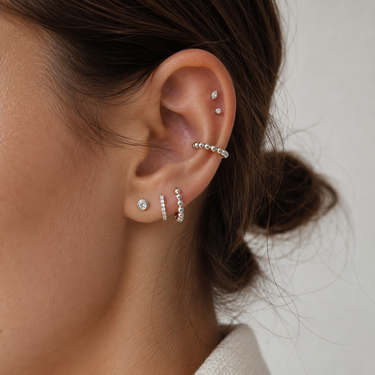 Close-up of an ear wearing multiple silver earrings with a neutral background