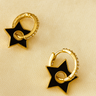 Black Star Huggie Earrings — gold-plated hoops with black enamel star charms, polished mirror finish on beige linen background, Matte Jewelry Collection.