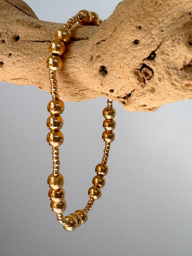 Single gold Blasco Bracelet with round beads draped over wood branch