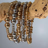 Stack of gold and silver Blasco Bracelets displayed on natural wood branch