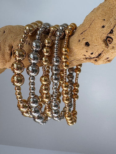 Stack of gold and silver Blasco Bracelets displayed on natural wood branch