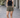 Woman wearing a black tank top and patterned shorts standing on a paved walkway.