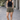 Woman wearing a black tank top and patterned shorts standing on a paved walkway.