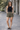 Woman wearing a black tank top and patterned shorts standing on a paved walkway.