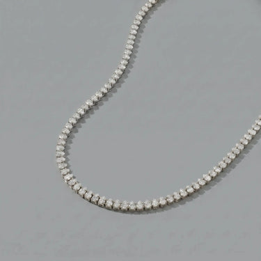 Silver teardrop tennis necklace with sparkling clear stones on a soft light gray background, photographed in a clean luxury jewelry editorial style with delicate reflections and minimal shadows.
