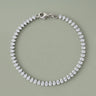 Silver teardrop tennis bracelet with sparkling clear stones and a polished silver clasp on a soft sage gray background, photographed in a clean luxury jewelry editorial style with refined reflections and minimal shadows.
