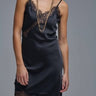 Black satin slip dress with delicate lace trim and fluid silhouette, shown on model layered with gold jewelry — Cala Dress by Matte.
