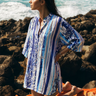 Capri Cover Up blue and white striped beach cover-up with relaxed tunic silhouette, long sleeves, and V neckline worn over swimwear by the ocean.