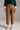 Front view of caramel relaxed fit cotton trousers with mid-rise waist and ankle length, styled with sneakers and green sweater